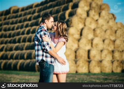 a guy with a girl on a summer walk in the field near round haystacks