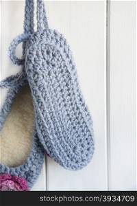 A Hand Crocheted Pair of Slippers Hanging Against A Wooden Door.