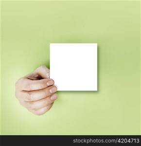 A hand holding a blank note over green background.