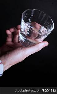 A hand holding a clear glass of water on a black background close up