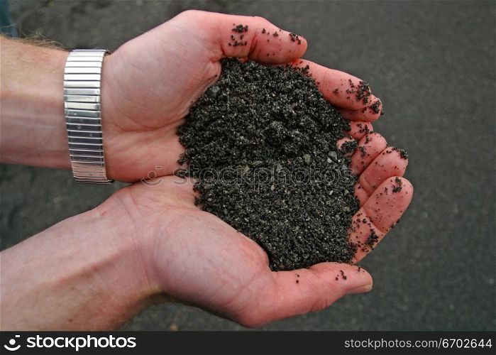 A hand holding black volcanic soil.