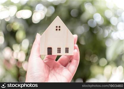 A hand holding model of wooden house with blur bogeh background