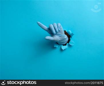 a hand in a blue medical glove is sticking out of a torn hole in a blue paper background, the index finger is raised. Part of the body indicates the direction