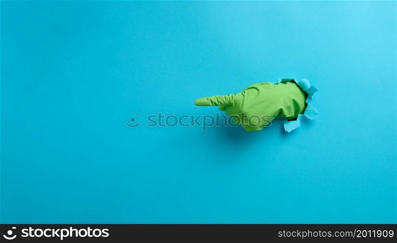 a hand in a green latex glove points a finger on a blue background. Place for inscription of discounts, offer or announcement.