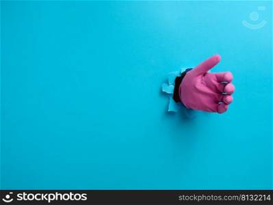 a hand in a pink latex glove holds an object, a part of the body sticks out of a torn hole in a blue paper background