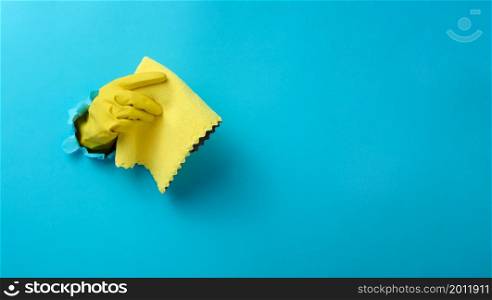 a hand in a yellow rubber cleaning glove holds a dry rag on a blue background. Part of the body stick out of the hole in the paper, banner