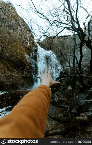 A hand in front of a massive waterfall on moody tones with liberty concept and travel on vintage tones with copy space