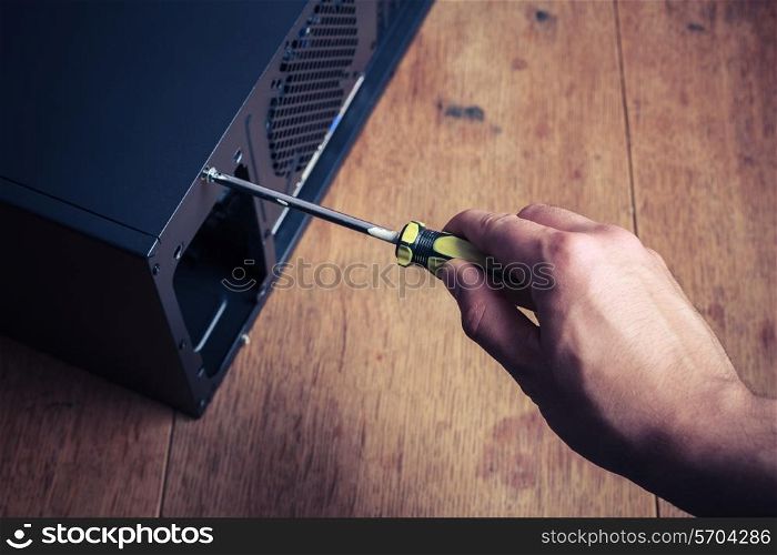 A hand is opening a computer case with a screwdriver