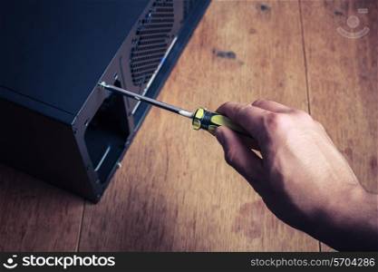 A hand is opening a computer case with a screwdriver