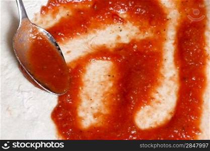 A hand smearing out pizza sauce
