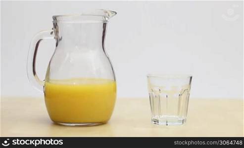 a hand takes the juice jar and pours a glass with orange juice, eine Hand nimmer einen Krug Orangensaft und fullt ein Glas damit