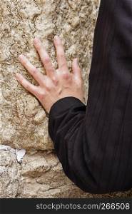 A hand touches the Wailing Wall in the Kotel during a prayer by an anonymous man in the Old City of Jerusalem.