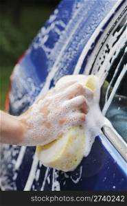 A Hand washing a blue car with a sponge