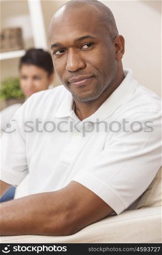A handsome African American man sitting thoughtful at home with his girlfriend or wife behind him