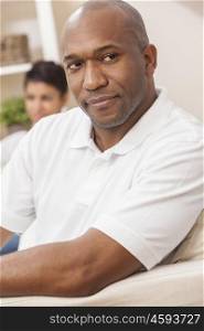 A handsome African American man sitting thoughtful at home with his girlfriend or wife behind him