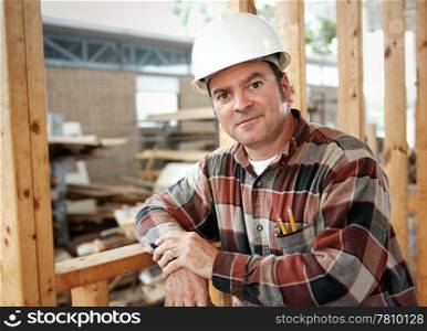 A handsome construction worker leaning on the frame of a building he&rsquo;s working on. Authentic construction worker photographed on site.