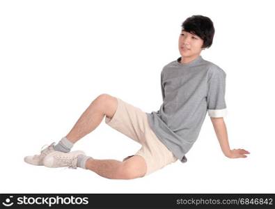 A handsome pretty young Asian teenager sitting in shorts on thefloor, smiling, isolated for white background.