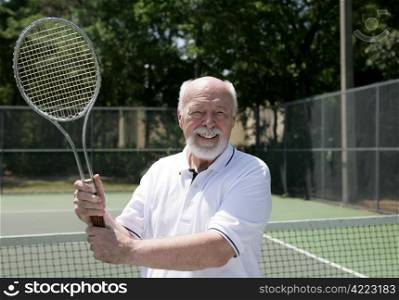 A handsome senior man on the tennis court getting ready for a game.