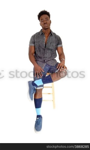 A handsome young African American man in shorts and sneakers sittingon a chair looking serious, isolated for white background.