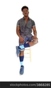 A handsome young African American man in shorts and sneakers sittingon a chair looking serious, isolated for white background.