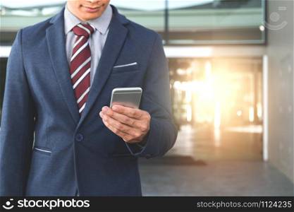 A handsome young businessman holding while using his phone and standing on the street.