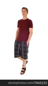 A handsome young man in a burgundy t-shirt and checkered shorts standing with his hands in the pockets, isolated for white background.