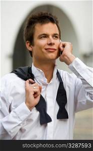 A hansdsome young man dressed in a dress shirt and black bow tie makes a call on his mobile phone