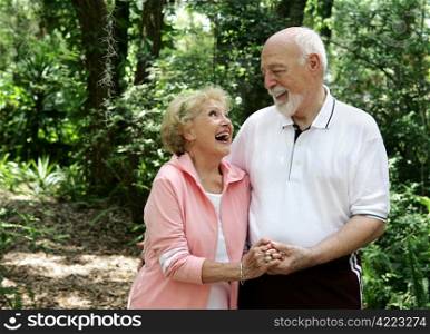 A happy, active senior couple laughing together on a walk through the park. She&rsquo;s wearing a hearing aid. Plenty of copyspace.