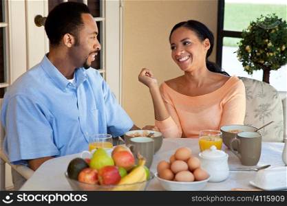A happy African American man and woman couple in their thirties sitting outside having a healthy breakfast