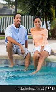 A happy African American man and woman couple in their thirties sitting wth their feet in a swimming pool