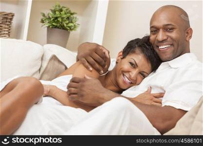A happy African American man and woman couple in their thirties sitting at home together smiling.