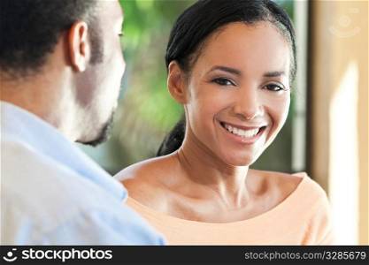 A happy African American man and woman couple sitting outside together with the woman smiling to camera.