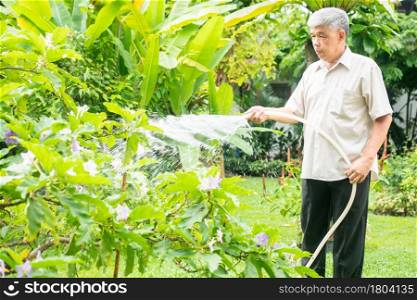 A happy and smiling Asian old elderly man is watering plants and flowers for a hobby after retirement in a home. Concept of a happy lifestyle and good health for seniors.