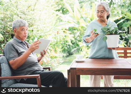 A happy and smiling Asian old elderly woman is planting for a hobby after retirement and her husband is reading a book. Concept of a happy lifestyle and good health for seniors.