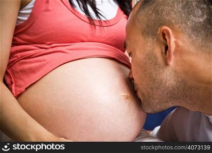 A happy asian father to be kissing his pregnant wife on the tummy