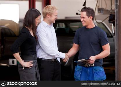 A happy attractive mechanic shaking hands with a customer couple,happy with their service