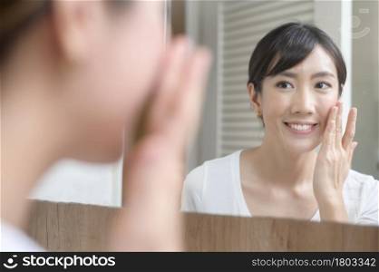 A happy beautiful woman applying moisturizing cream on face, skin care and treatment concept. Happy beautiful woman applying moisturizing cream on face, skin care and treatment concept