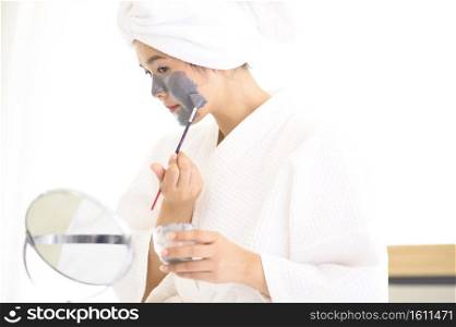 A happy beautiful woman in white bathrobe applying a face mask, skin care and treatment concept. Happy beautiful woman in white bathrobe applying a face mask, skin care and treatment concept