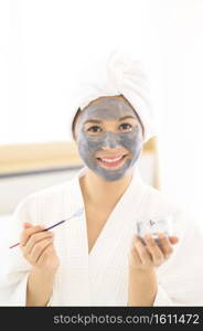 A happy beautiful woman in white bathrobe applying a face mask, skin care and treatment concept. Happy beautiful woman in white bathrobe applying a face mask, skin care and treatment concept