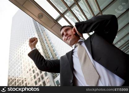 A happy businessman talking on his cell phone with his arm out stretched in a modern city environment and surrounded by office buldings