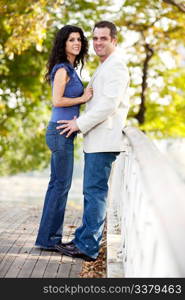 A happy couple in a park on a bridge looking at the camera