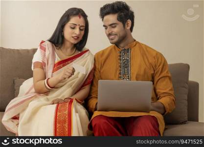 A HAPPY COUPLE IN TRADITIONAL CLOTHING LOOKING AT EACH OTHER WHILE DOING ONLINE TRANSACTION