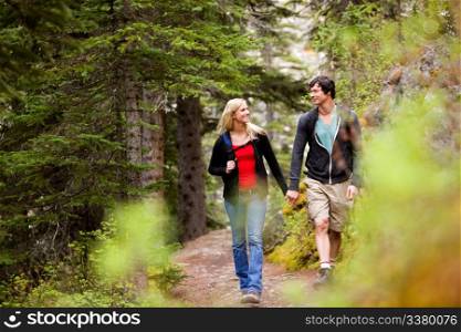 A happy couple looking at eachother and walking in the forest holding hands