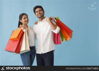 A HAPPY COUPLE POSING IN FRONT OF CAMERA WITH SHOPPING BAGS IN HAND