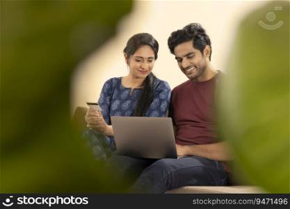 A HAPPY COUPLE SITTING AT HOME AND DOING ONLINE TRANSACTION