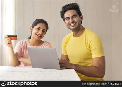 A HAPPY COUPLE SITTING AT HOME AND DOING ONLINE TRANSACTION