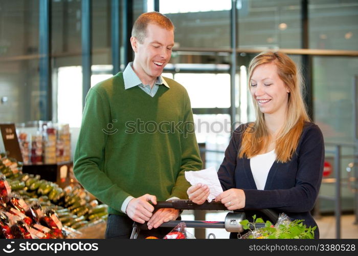 A happy couple with a shopping cart and grocery list in a supermarket