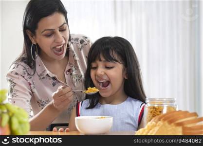 A HAPPY DAUGHTER CHEERFULLY EATING CORNFLAKES GIVEN BY MOTHER