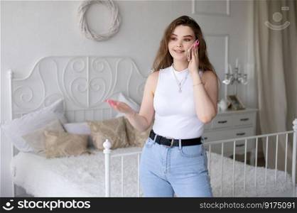 A happy European woman has a video call on her smartphone . The girl looks into the phone camera and smiles. White Scandinavian interior. Daylight through the window.. An excited successful European woman with a phone raises her hands. A remote worker in her apartment.