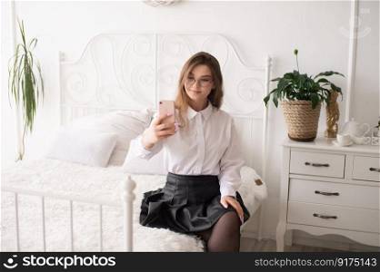 A happy European woman has a video call on her smartphone . The girl looks into the phone camera and smiles. White Scandinavian interior. Daylight through the window.. A happy woman has a video call. The girl looks into the phone camera and smiles.